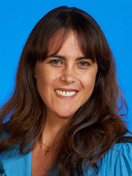 Smiling person with long brown hair against a blue background, wearing a blue top.