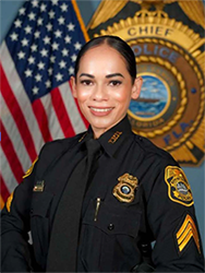 Police officer smiling in front of a U.S. flag and police insignia.