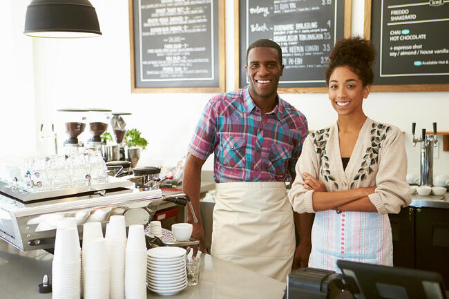 Female coffee shop owner and male employee smiling behind the counter.