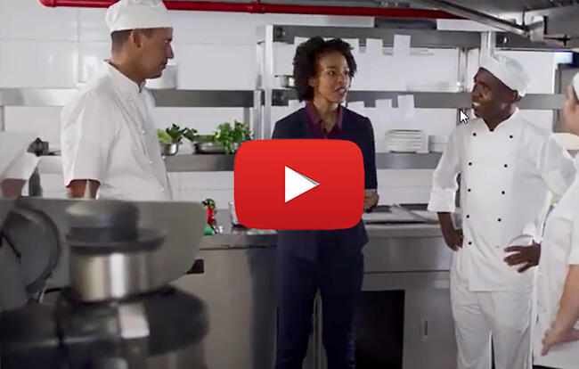 Chefs and staff in a kitchen engaged in a conversation, possibly in a hospitality context.