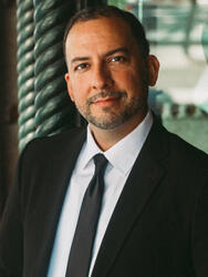 Man in a black suit and tie, posed near a twisted column.