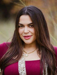 Woman smiling outdoors, wearing a burgundy top and a necklace.