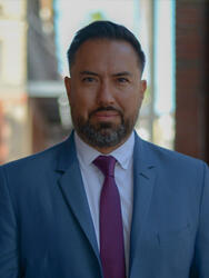 Man in a blue suit and pink tie, standing on a city street.