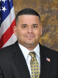 Man in a suit with a U.S. flag backdrop, named Rafael Pizano.