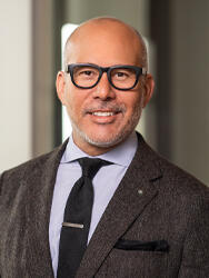 Ray Wong, wearing glasses and a suit, smiling in a professional setting.