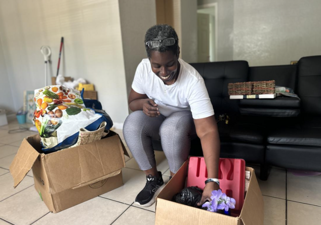 Woman organizing items in boxes, smiling, sitting on the floor in a living room.