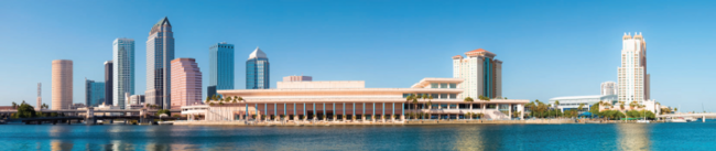 Tampa Convention Center on a clear day with blue sky and water reflection.