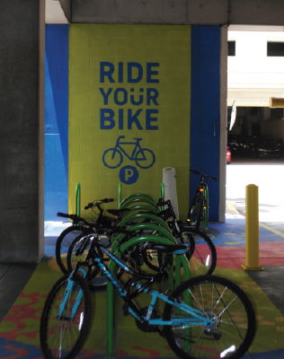 Bike parking area with green and blue mural reading "Ride Your Bike,"