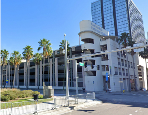 Multi-level parking garage with palm trees and a tall building, sunny day.