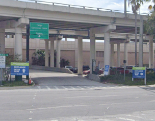 Underpass with road signs at a highway entrance, with cars and palm trees nearby