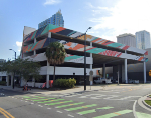 Colorful geometric mural on a multi-level parking garage, city skyline backdrop.