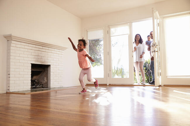 Family excitedly explores a new home, child running inside.