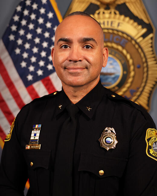 Deputy Chief DeFelice in uniform with badges, U.S. flag and police emblem background.