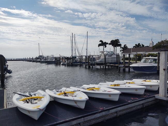 Small sailboats docked in a coastal marina under a partly cloudy sky.