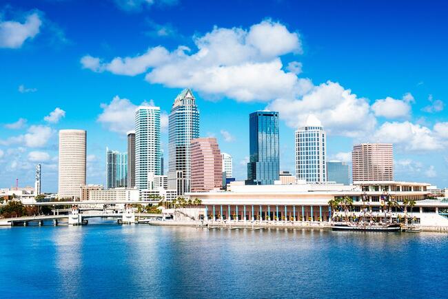City skyline with tall buildings and waterfront, under a blue sky.