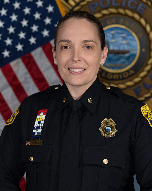 Photograph of Major Whitney McCormick in police uniform, U.S. flag and police emblem behind.