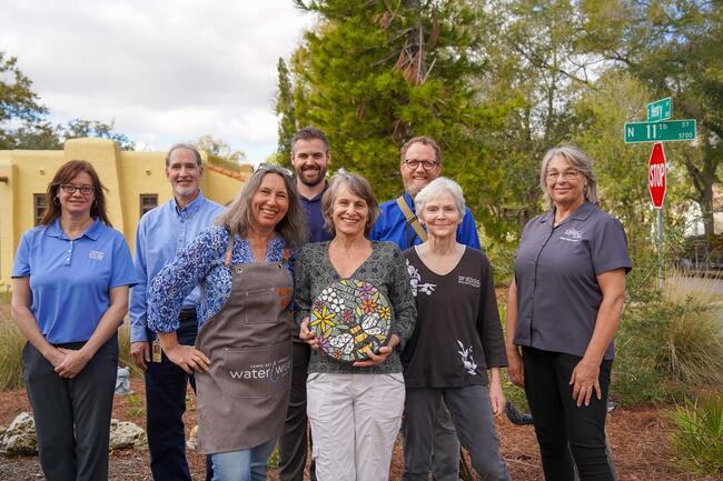 Susan Manian, one of the 2025 Community Water Wise Award winners, holding his awarded round Waterwise 2025 mosaic stone. Liselott Uppgard who is on Susan's left, is the runner up and won a WaterWise apron. Behind them are the judges for this award.