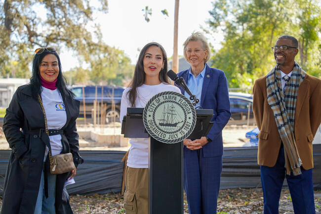 Four people at a podium outdoors for Infill Phase 3 construction announcement.
