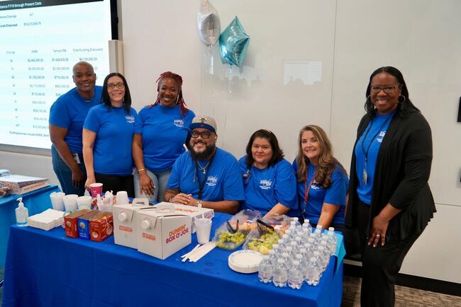 Group of people at a homeownership event 2026, smiling behind a table with food and drinks.