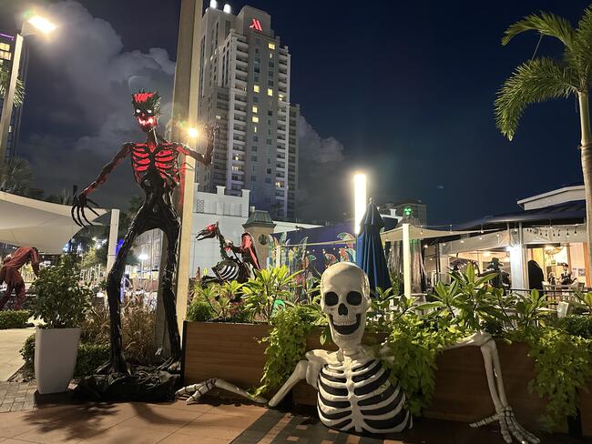 Large skeleton and demon Halloween decorations in an outdoor urban plaza at night.