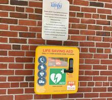 Life-saving AED cabinet on a brick wall with emergency instructions.