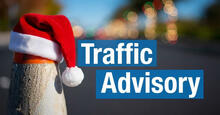 Traffic cone with Santa hat beside text "Traffic Advisory" on road.