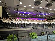 Large choir in formal attire performing on stage, January 2025 event.