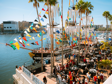 Colorful pirate festival with crowded dock, ships, and festive flags, likely Gasparilla 2026.