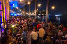 Crowded nighttime waterfront gathering with string lights overhead.