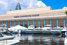 Photo of the Tampa Boat Show at the Tampa Convention Center. Boats/Yachts are docked outside, the sky is blue in the background with white clouds.