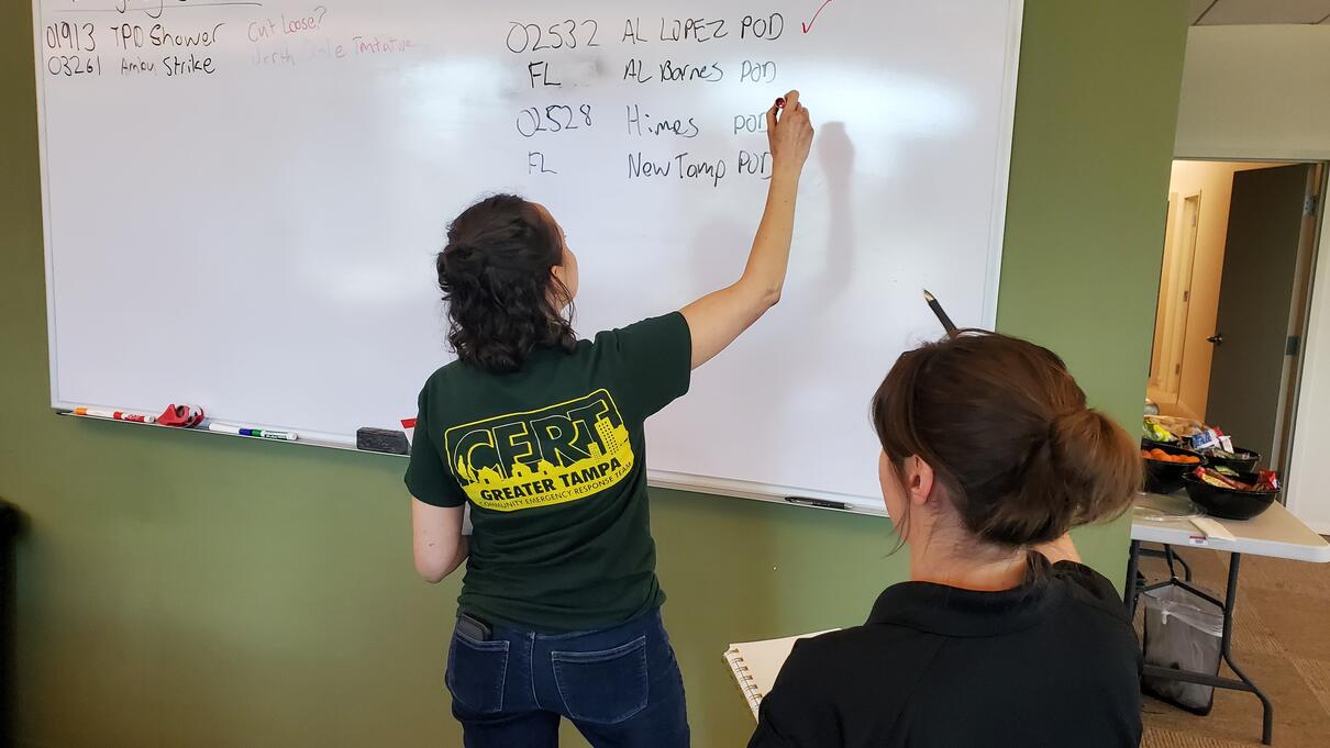 Two people writing and taking notes on a whiteboard in a classroom setting.