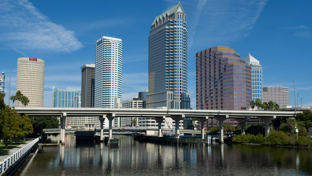 Downtown Tampa skyline with modern high-rise buildings and clear blue sky reflected in the river.