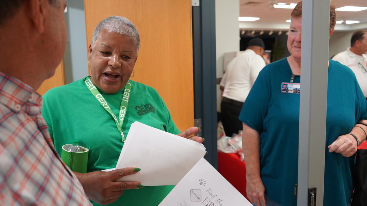 People discussing papers in an office setting, one wearing a green shirt.