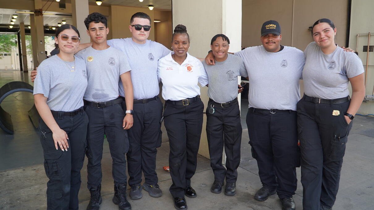Six people in matching uniforms pose together outside a building, smiling at the camera.
