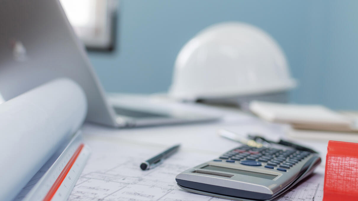 Calculator, blueprints, and a hard hat on an architect’s desk.
