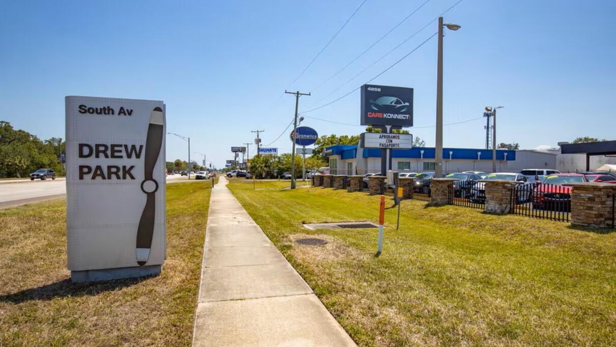 Drew Park, Tampa, FL sign by a street with clear blue sky and nearby businesses.