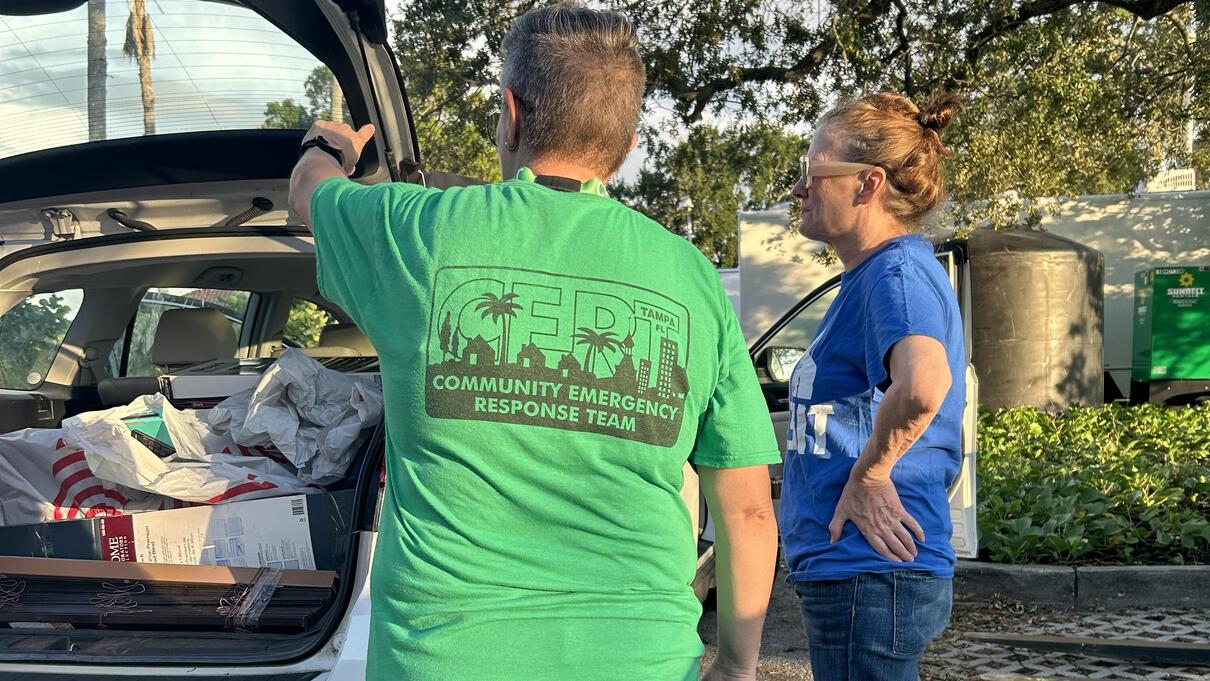 Two people near an open car trunk, one wears a green shirt with "50th Conference Response Team" text.