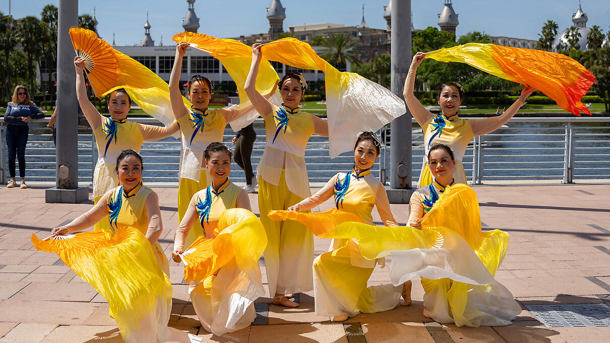 Dancers in colorful costumes perform near a river in Tampa, celebrating Asian Pacific culture.