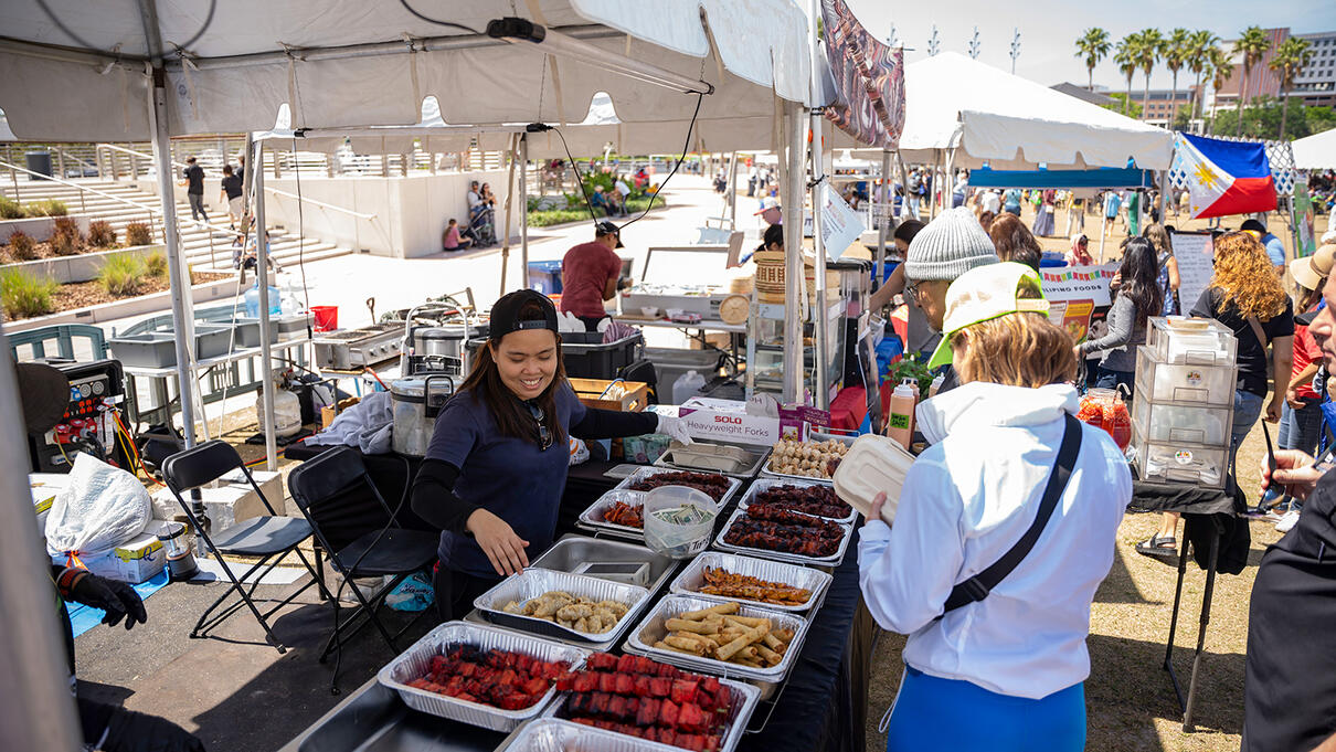 Food vendor at an outdoor Tampa Asian Pacific festival, serving assorted dishes under a tent.