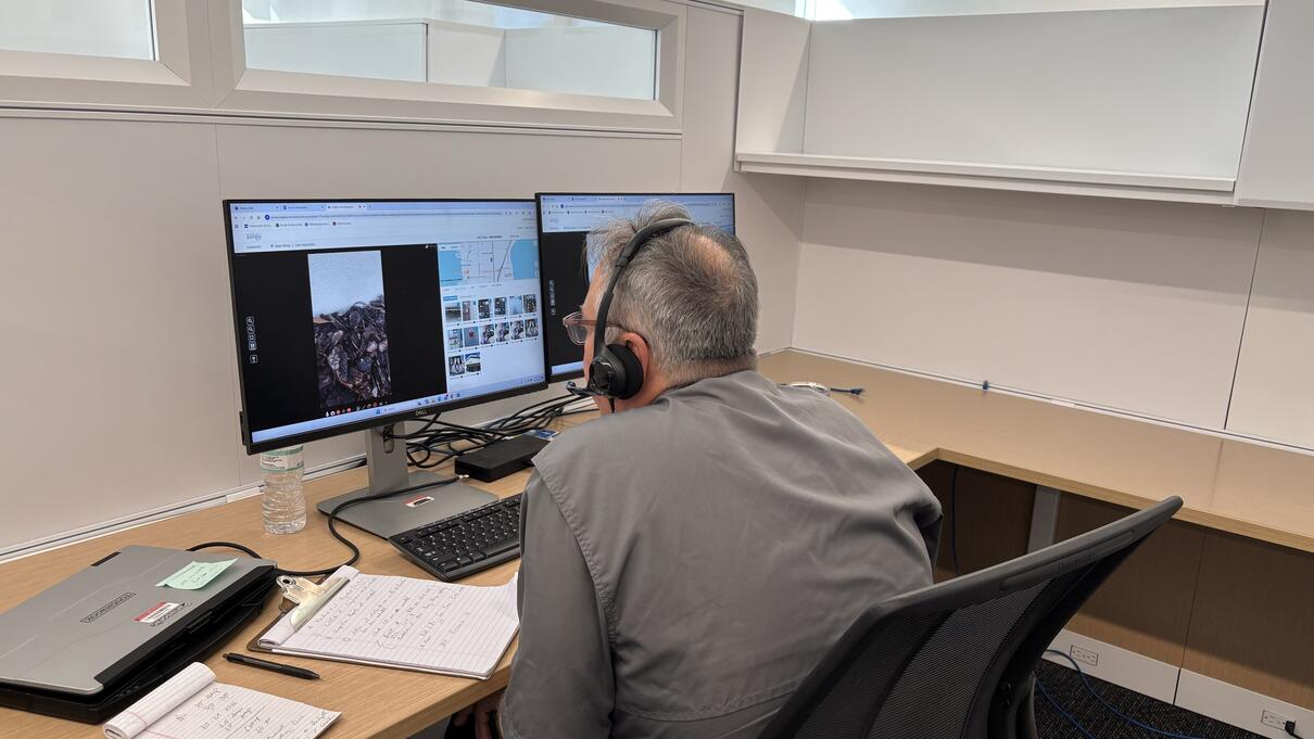 Person conducting a virtual inspection using dual monitors and video call in an office setting.